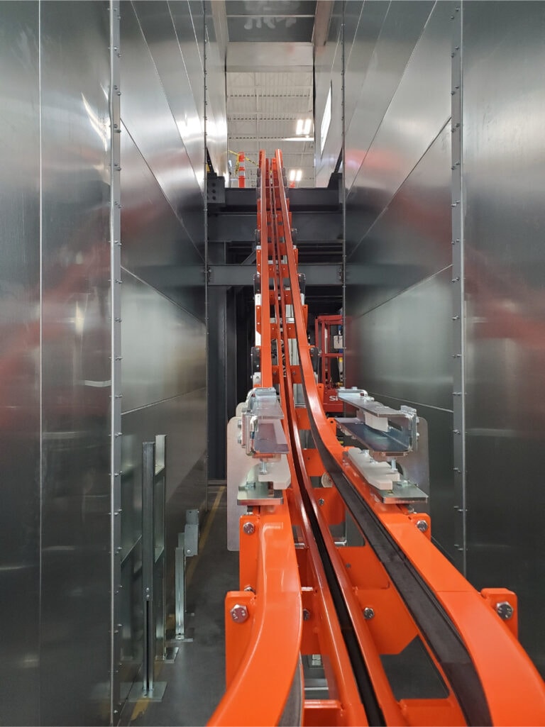System construction — spray booth interior with orange conveyor track curving through tunnel